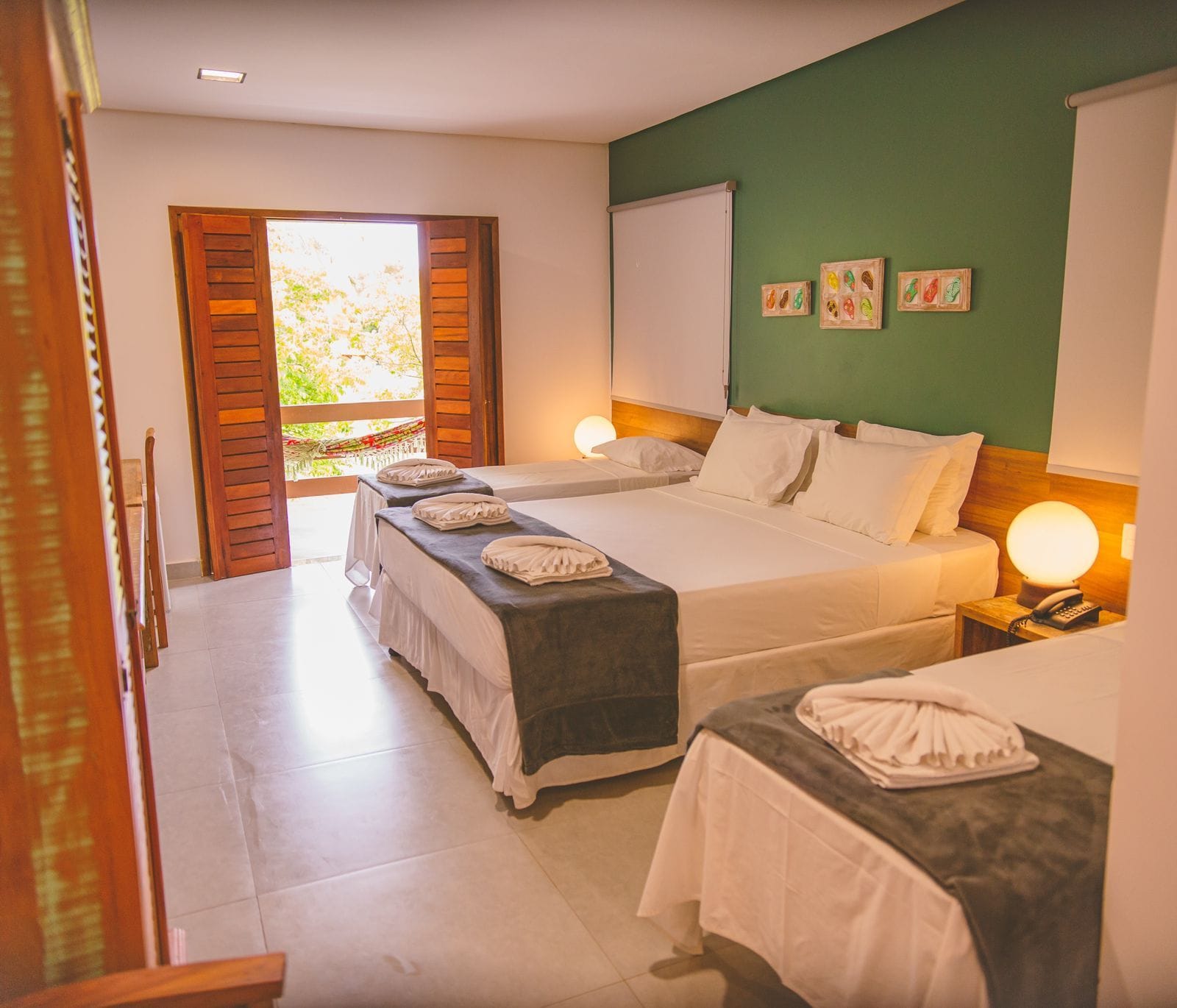 Une chambre d’hôtel avec deux lits, un balcon, un tableau blanc et un mur décoré de tableaux.