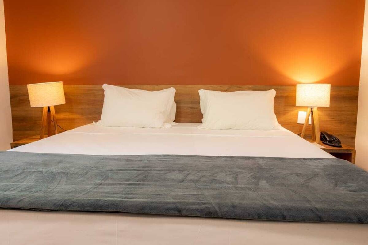 Een net opgemaakt bed met een grijze plaid, twee witte kussens en twee bedlampjes op houten nachtkastjes.