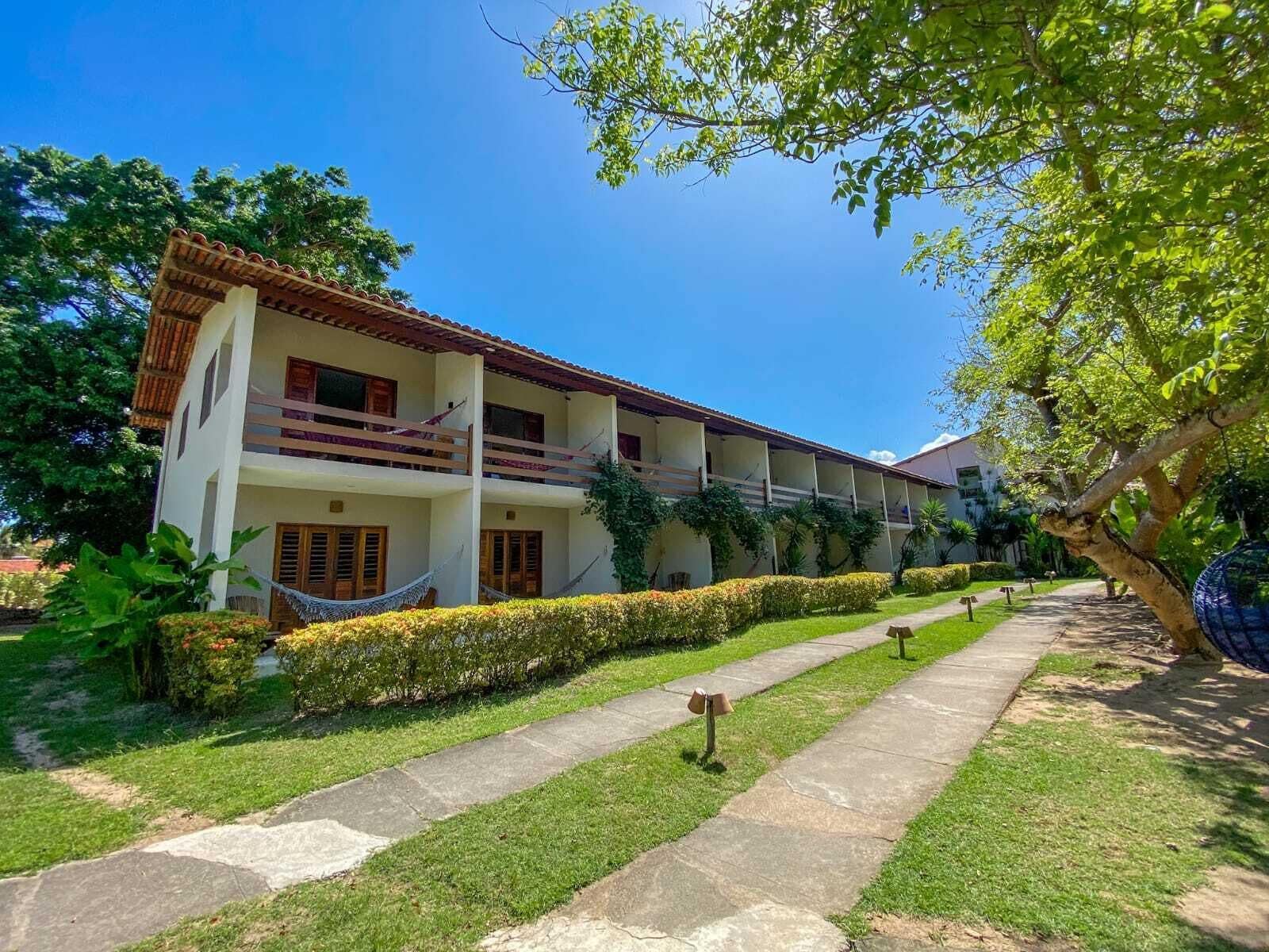 Un hotel de dos pisos con balcón en el piso superior, rodeado de jardines cuidados y un sendero despejado.
