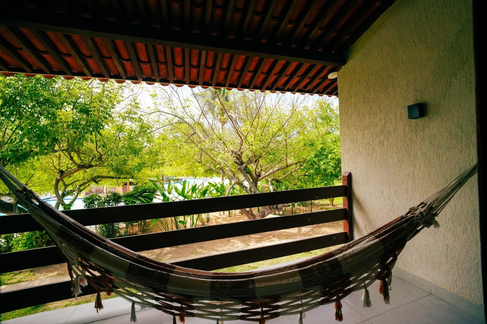 A hammock on a balcony with a view of trees and a building in the background.