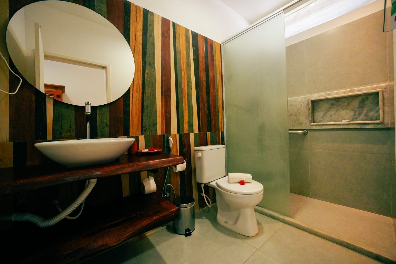 Une salle de bain avec un meuble-lavabo en bois, un lavabo blanc, des toilettes et un espace douche.