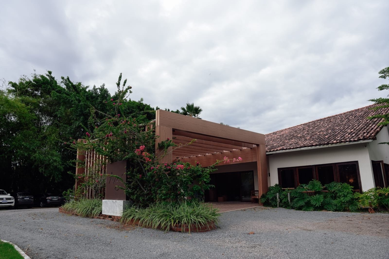 A modern building with a covered entrance, surrounded by lush greenery and a gravel driveway.