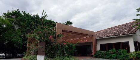 A modern building with a covered entrance, surrounded by lush greenery and a gravel driveway.