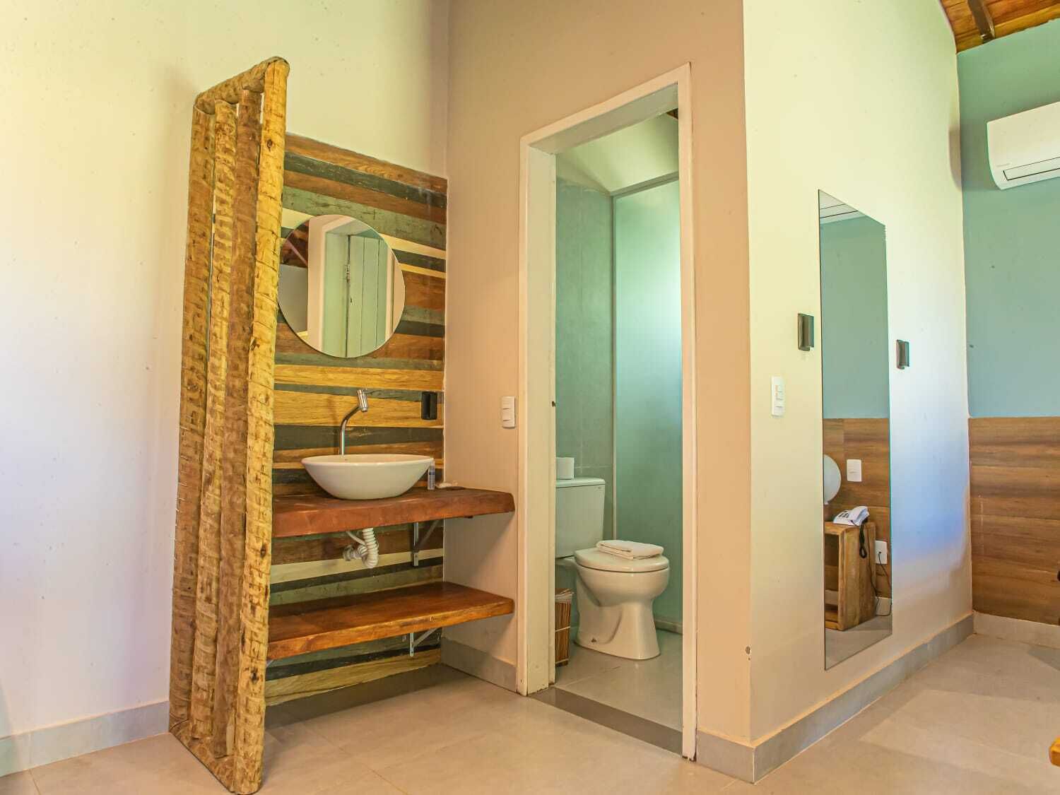 Une salle de bain avec un meuble-lavabo en bois, un évier et un miroir. Une porte donne accès à une pièce séparée où se trouvent les toilettes.
