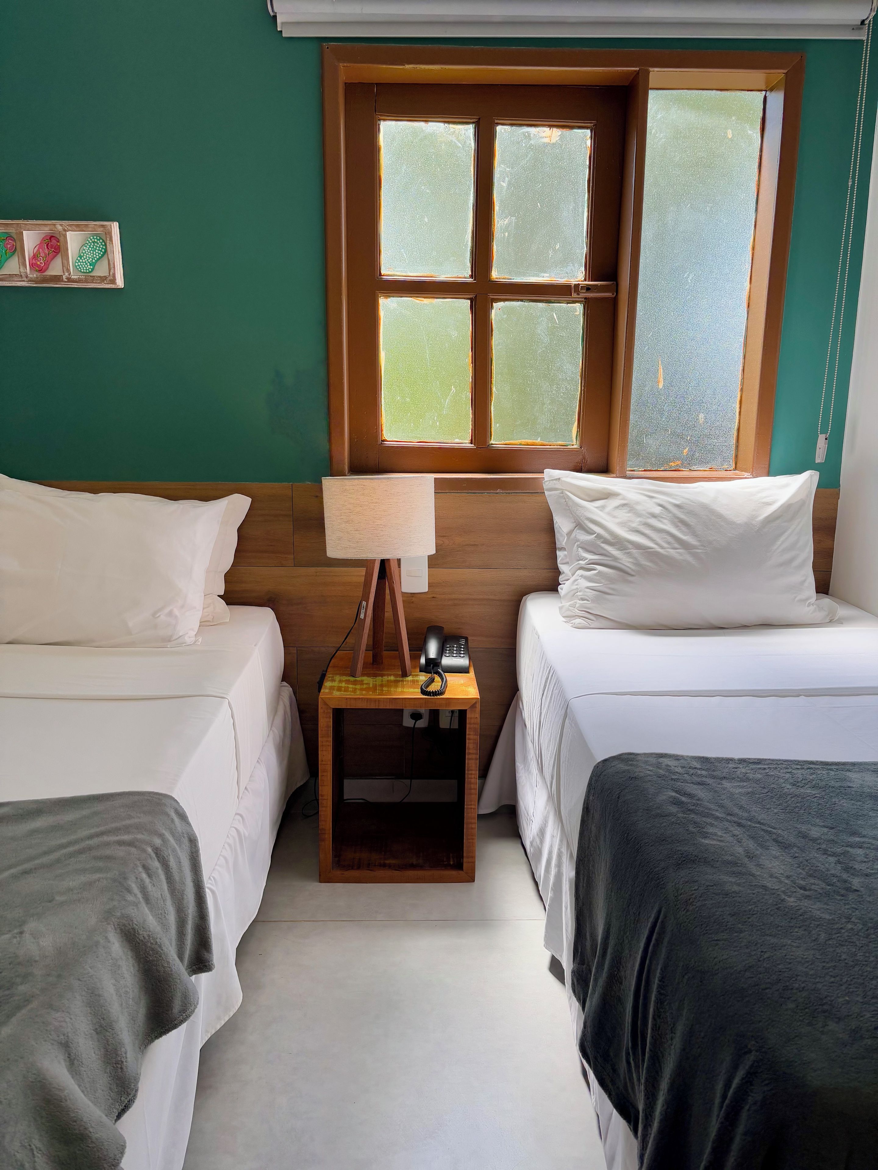A room with two beds, a wooden nightstand with a lamp, and a window with a view.