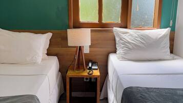 A room with two beds, a wooden nightstand with a lamp, and a window with a view.