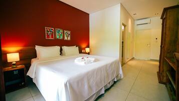 A hotel room with a large bed, two bedside tables with lamps, a wooden wardrobe, and a red accent wall with floral artwork.