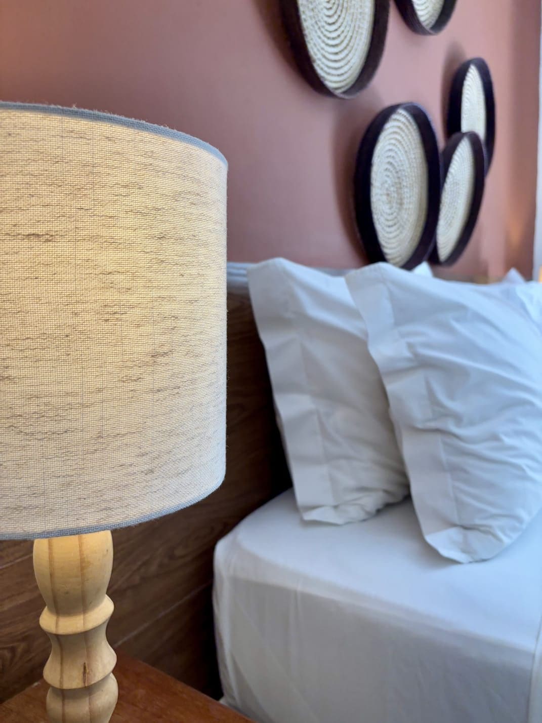 Una cama con ropa de cama blanca y una mesita de noche de madera con una lámpara.