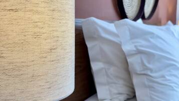 Una cama con ropa de cama blanca y una mesita de noche de madera con una lámpara.