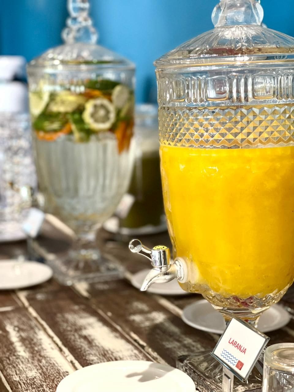 A beverage dispenser with a spout and a label, and a glass container with a lid in the background.