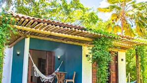 A small, single-story house with a tiled roof, a hammock, and a table and chair set outside.