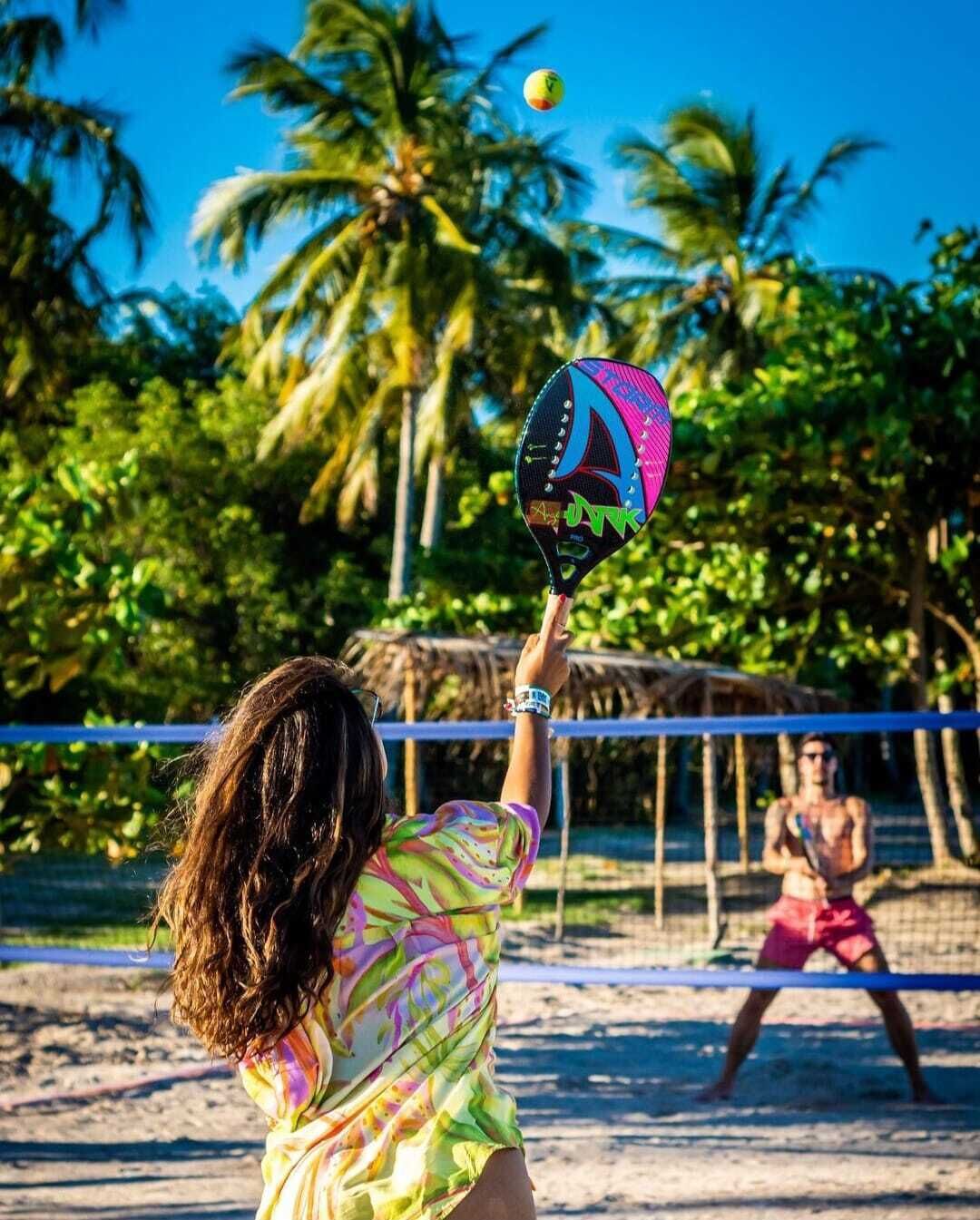 A person playing beach volleyball on a sandy court with palm trees in the background.