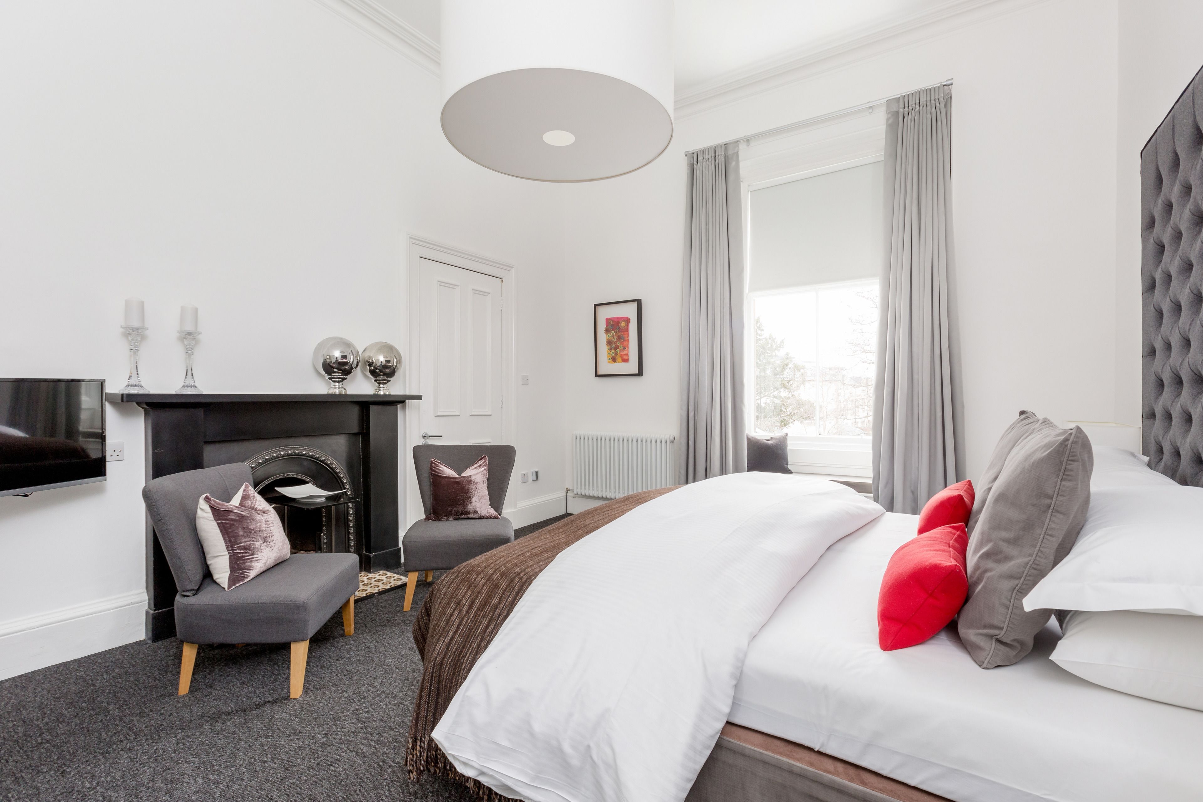 Une chambre d’hôtel moderne équipée d’un lit, de deux fauteuils, d’une cheminée et d’une grande fenêtre avec des rideaux.