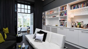A modern living room with a white sofa, black and yellow cushions, a bookshelf, and a glass cabinet with bottles. - 94DR (Edinburgh)