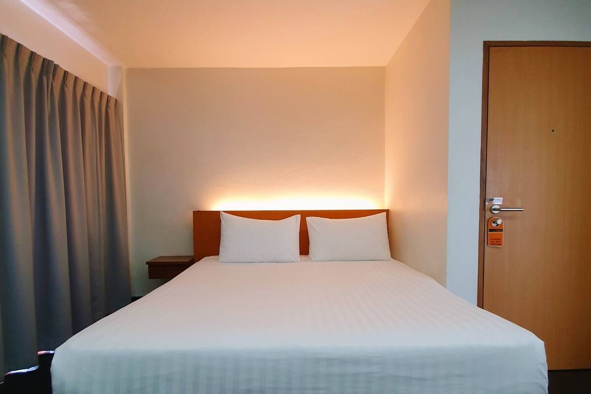 Une chambre d’hôtel avec un grand lit, une table de chevet, une porte en bois et un rideau.