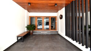 Un hall d’entrée moderne avec un plafond en bois, un banc, des plantes en pot et une porte en verre donnant accès à un bâtiment.