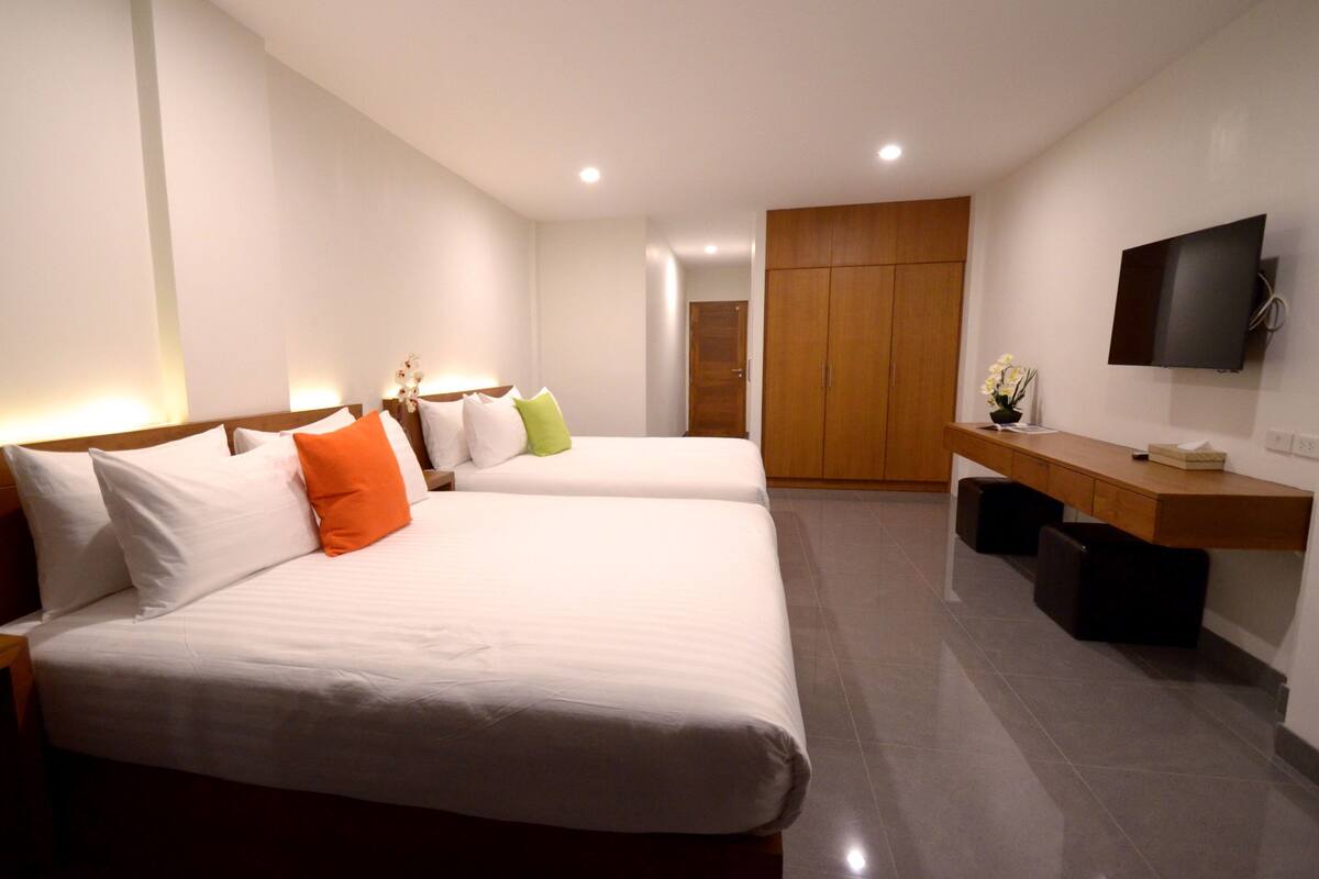 Une chambre d’hôtel avec deux lits, une tête de lit en bois, un bureau avec un téléviseur à écran plat et une armoire.