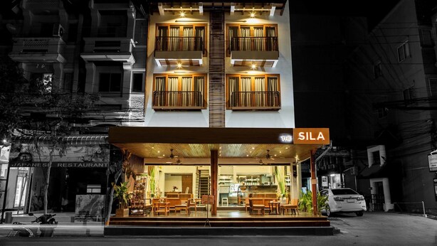 Un immeuble de deux étages abritant un restaurant appelé « SILA » au rez-de-chaussée. Le restaurant présente un design moderne, avec des meubles en bois et une entrée en verre.