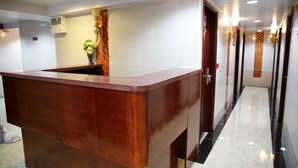 A reception desk with a wooden finish, a wall-mounted air conditioning unit, and a fire alarm sign on the wall. - Sandhu guest house (Kowloon)