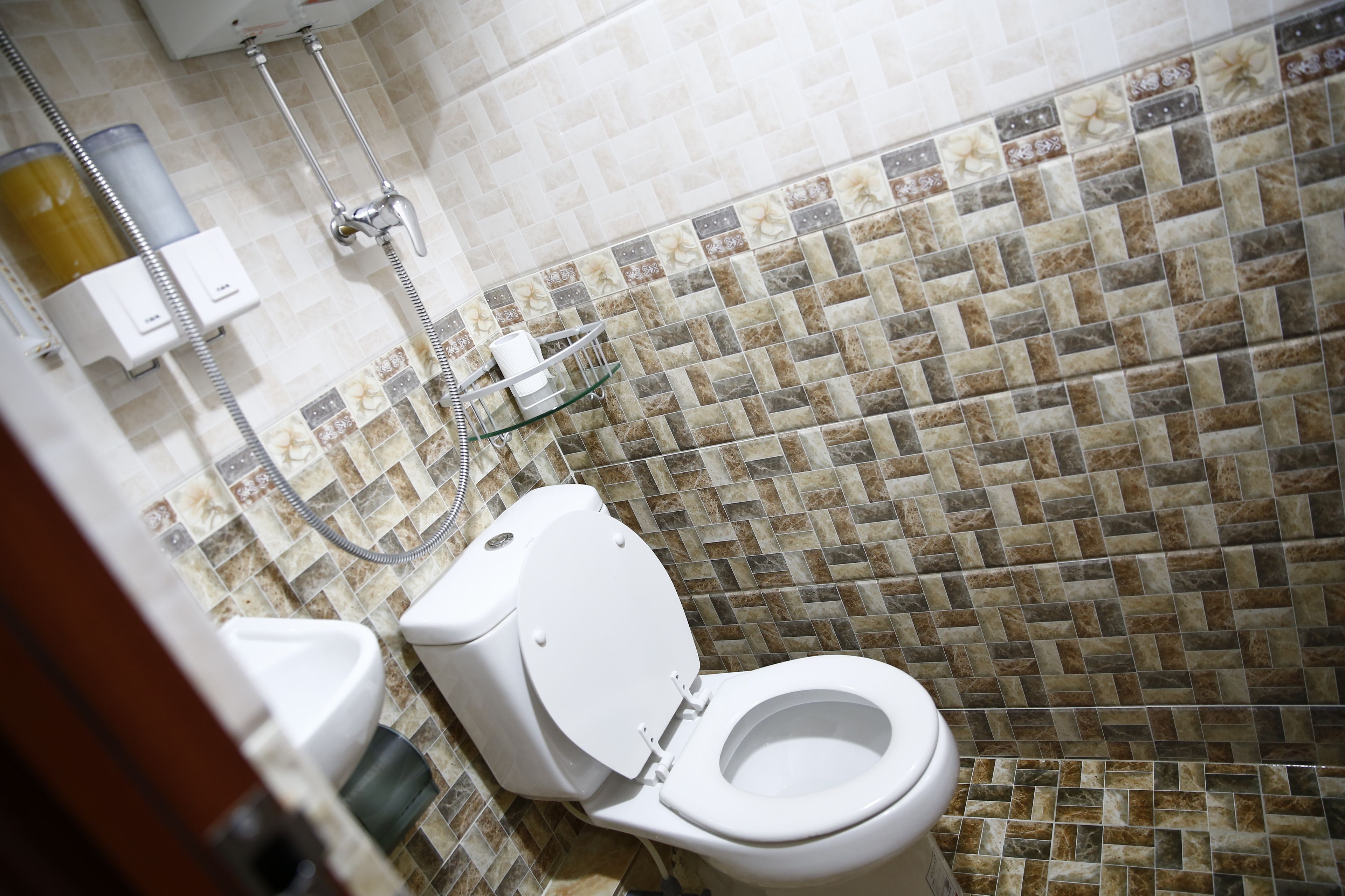 Un baño con inodoro blanco, ducha y pared con azulejos.