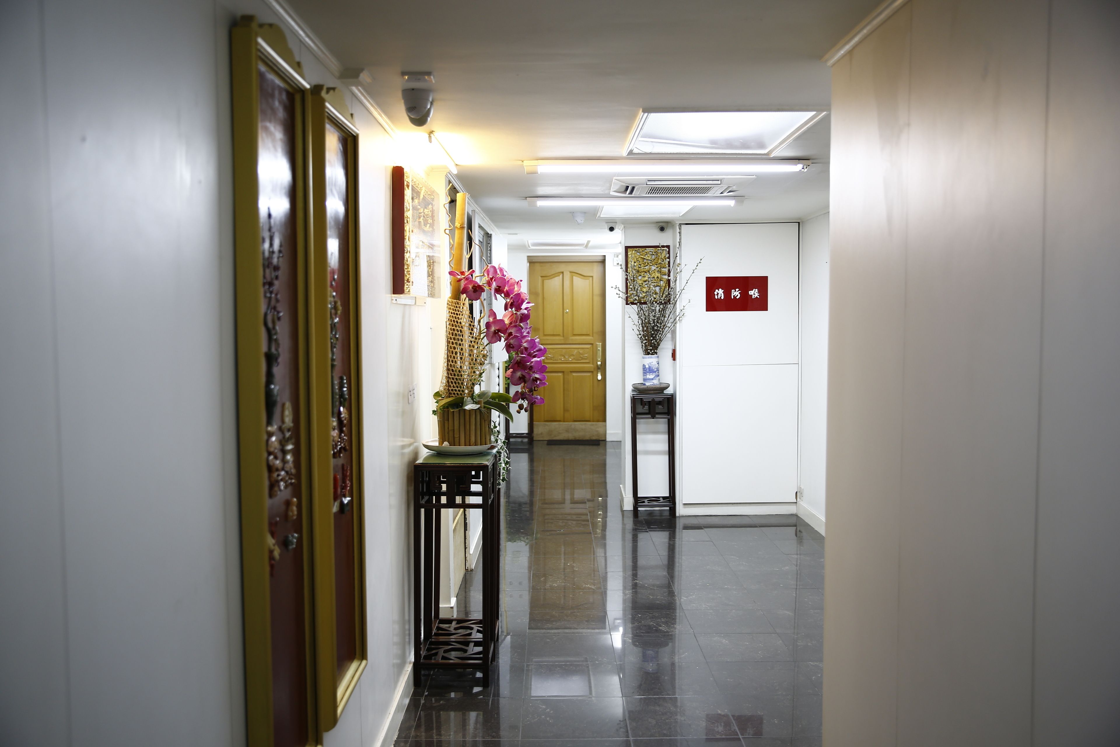 A hallway with a polished floor, a wooden door, and a small table with a vase of flowers.