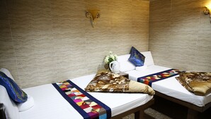 A hotel room with two beds, each with a white mattress and a colorful quilt. There is a decorative wall sconce above the beds and a small vase with flowers on the nightstand. - Sandhu guest house (Kowloon)