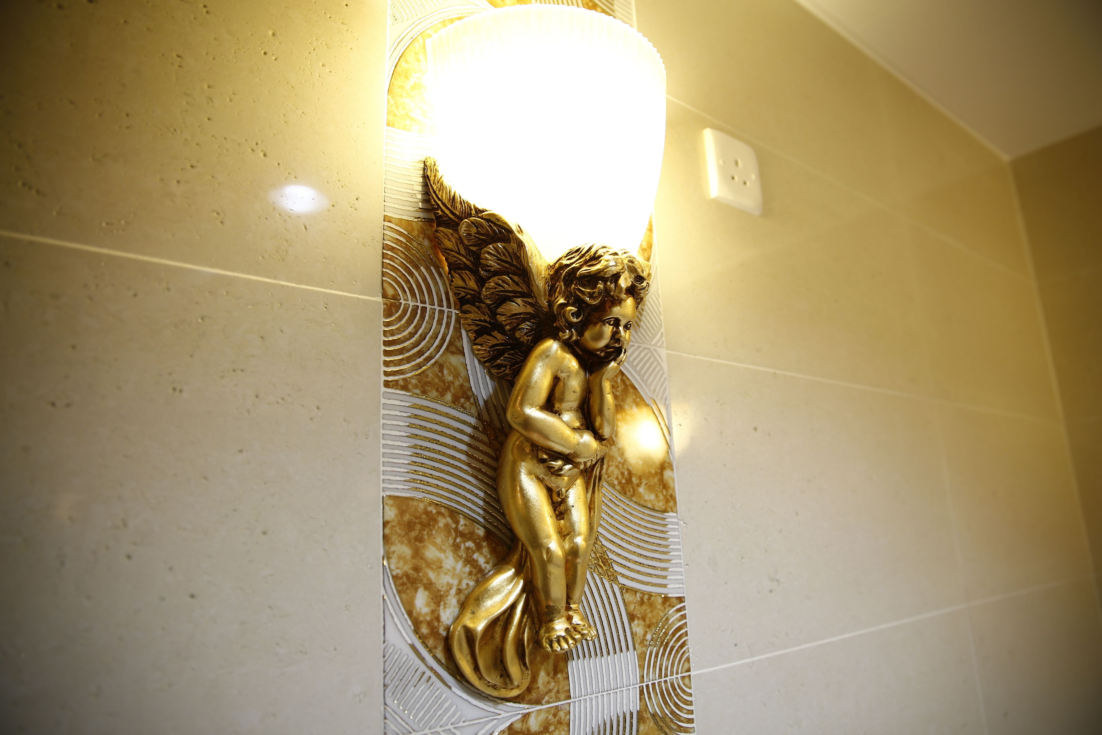 Estátua dourada de um querubim alado fixada em uma parede revestida de azulejos.