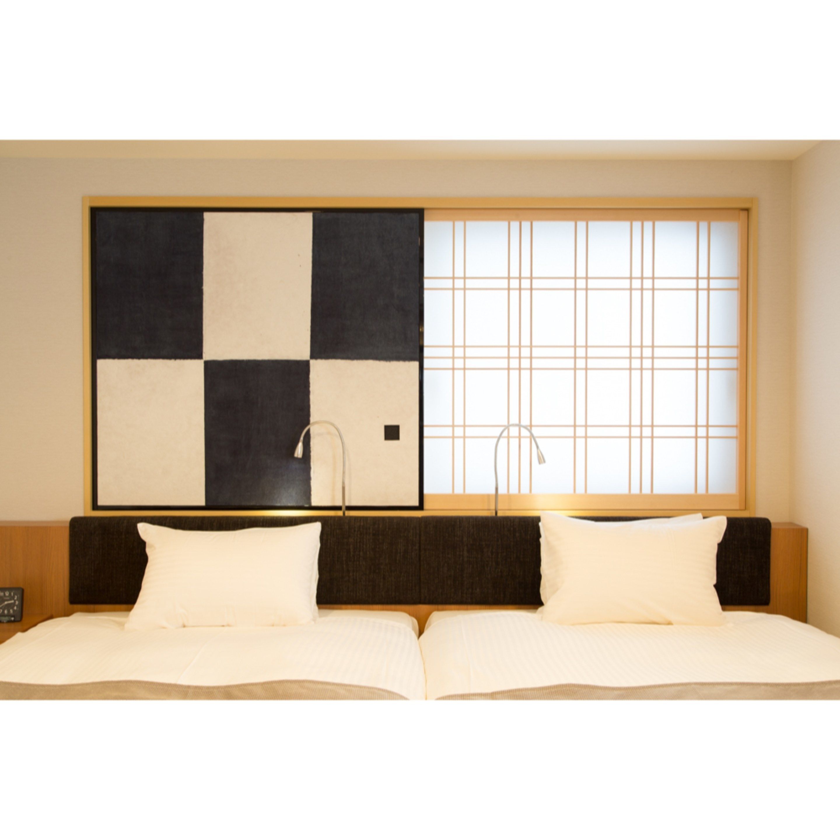 A hotel room with a large bed, a headboard with a dark panel, and a large window with a grid pattern.
