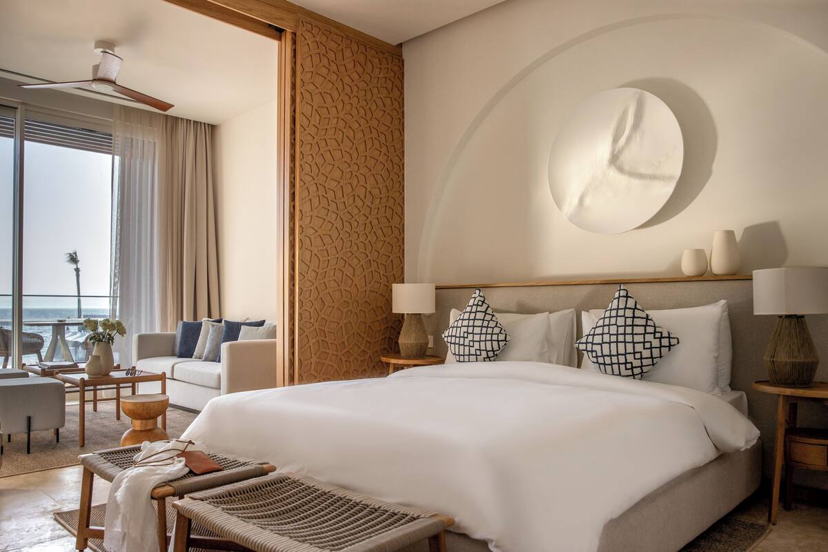 Een hotelkamer met een groot bed, een bank, een eettafel en uitzicht op de oceaan.