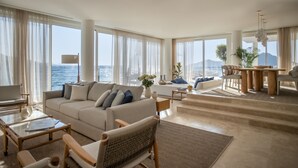 Een ruime woonkamer met een groot raam met uitzicht op zee, een comfortabele bank, een eettafel en een trap naar een hoger gelegen verdieping.