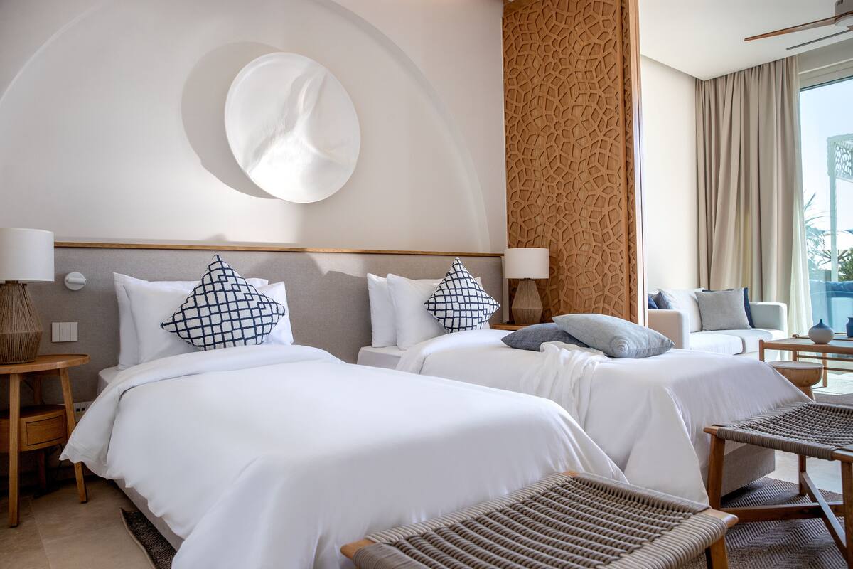 Een hotelkamer met twee bedden, een grote spiegel, een behang met patroon en uitzicht op de omgeving.