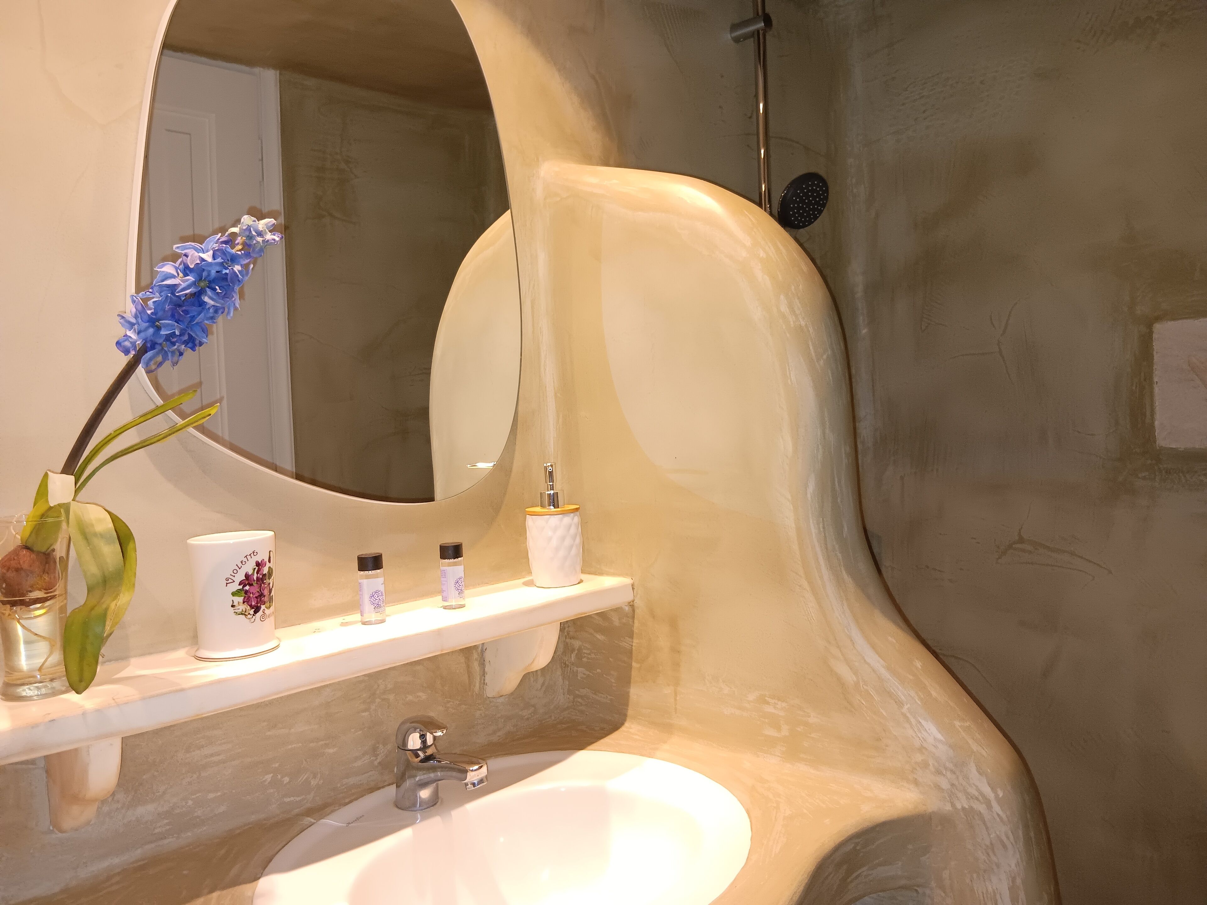 A bathroom with a white sink, a mirror, and a shelf with toiletries.