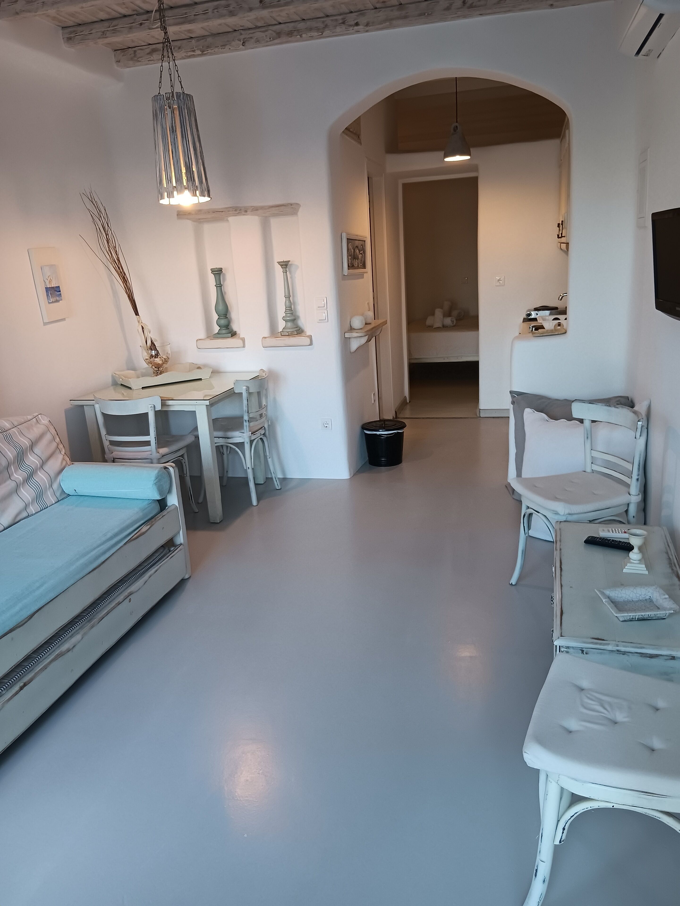 A cozy room with a bed, a desk, and a chair. There is a small table with a lamp and a picture frame.