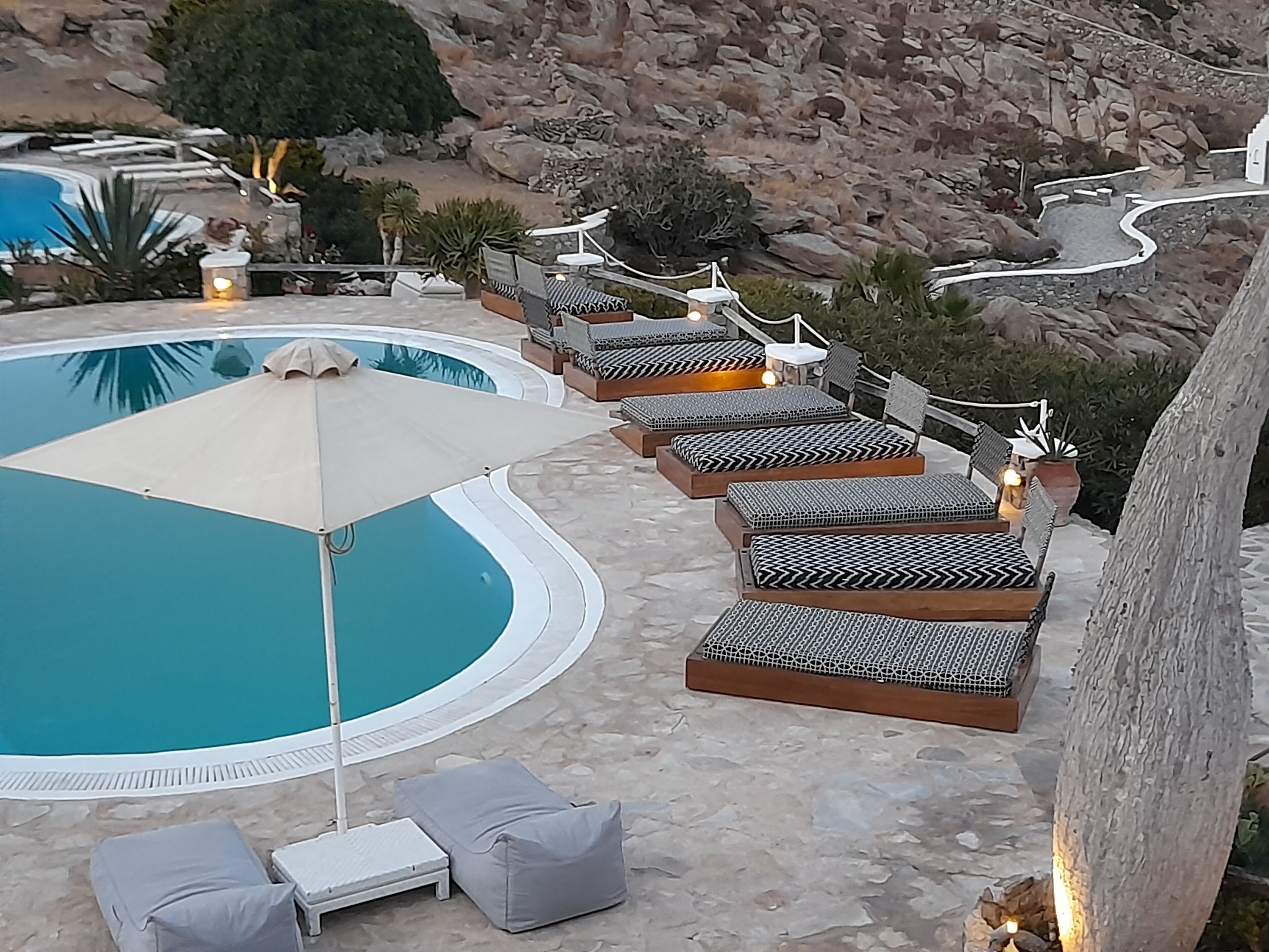 Un espace aménagé au bord de la piscine, avec des chaises longues et une table, le tout entouré d’un paysage rocheux.
