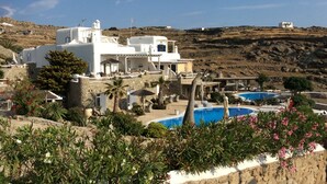 A white building with a pool, surrounded by greenery and hills. - Navy Blue Suites (Mykonos)