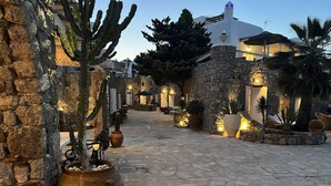 A stone courtyard with outdoor seating, potted plants, and a building with white walls and a blue roof. - Navy Blue Suites (Mykonos)