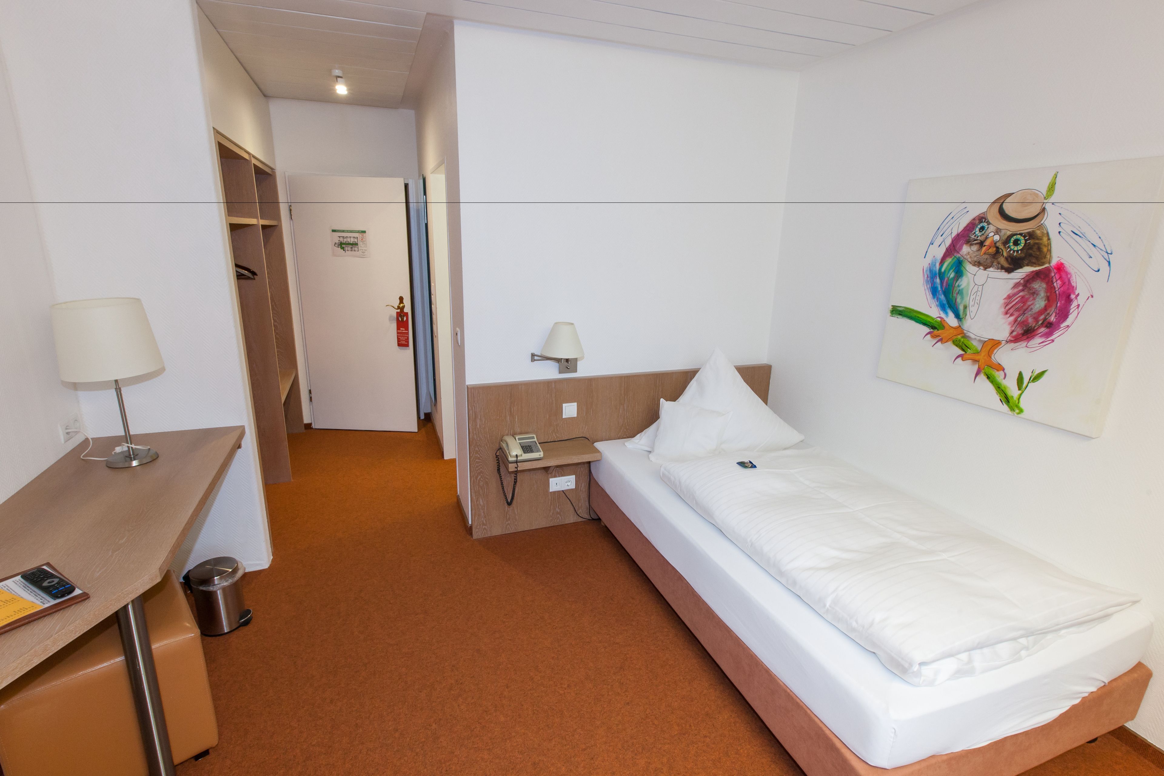 Una habitación de hotel con cama, mesita de noche, lámpara y un cuadro colgado en la pared.