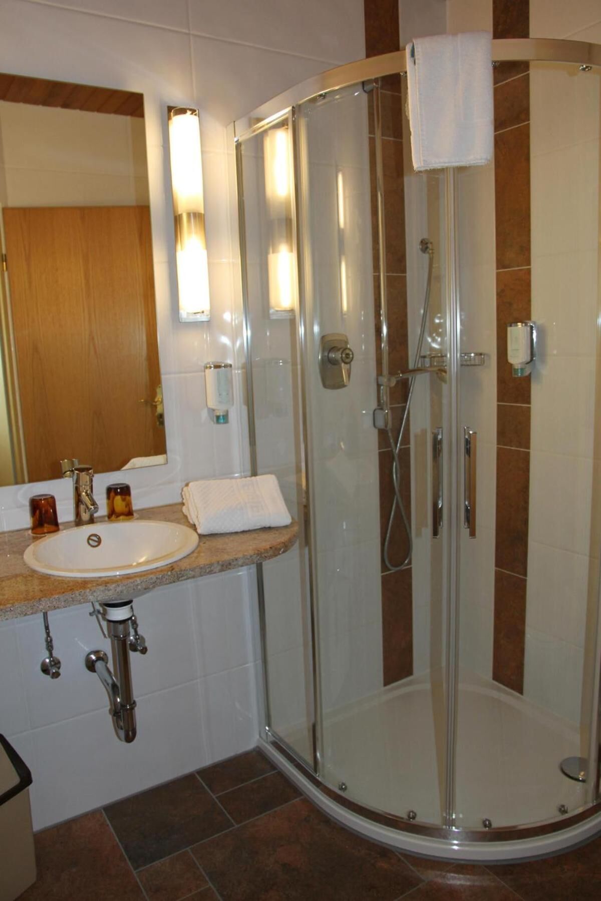 A glass-enclosed shower with a white towel hanging on the door, a sink with a mirror above it, and a wooden countertop.