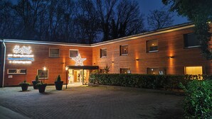 A hotel with a wooden facade, a large illuminated star, and a sign indicating a camping area. - Hotel am Springhorstsee (Burgwedel)