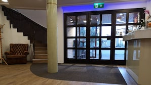 A reception area with a staircase, a leather armchair, and a large pillar. - Hotel am Springhorstsee (Burgwedel)