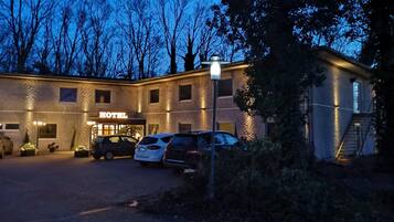 Un hotel con fachada de ladrillo, un cartel que dice "HOTEL" y varios coches estacionados al frente.