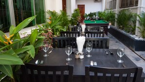 Un espace repas avec un billard, entouré de plantes en pot et agrémenté de sièges d’extérieur.