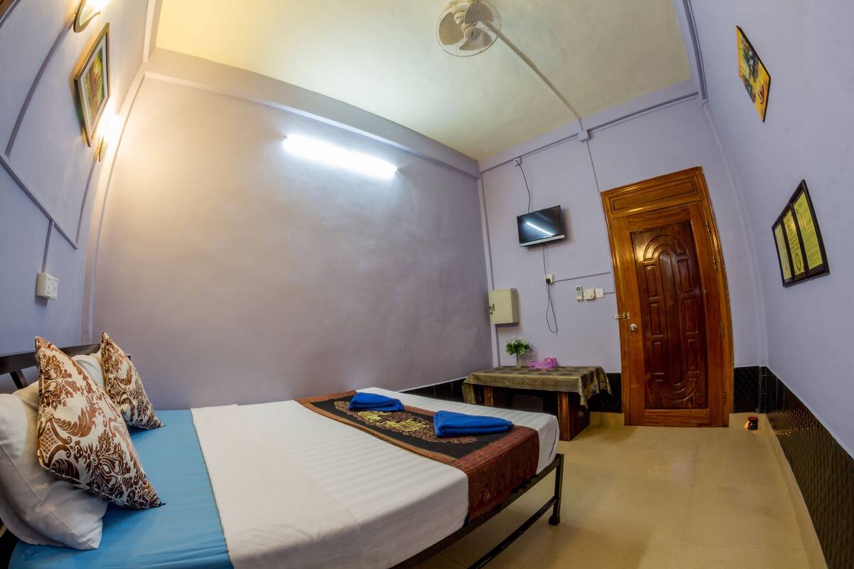 Een kamer met een bed, een bureau, een televisie en een deur.