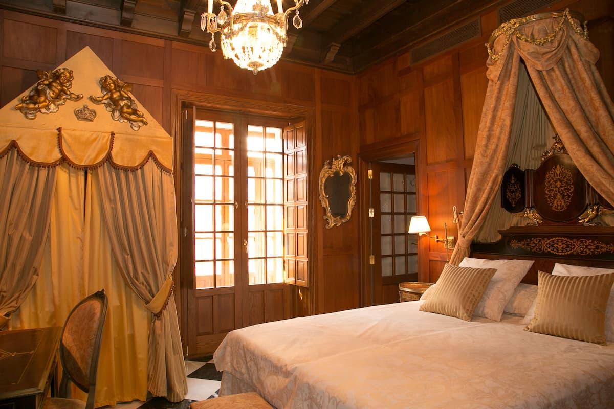A room with a large bed, a canopy bed, wooden paneling, a chandelier, and a mirror.