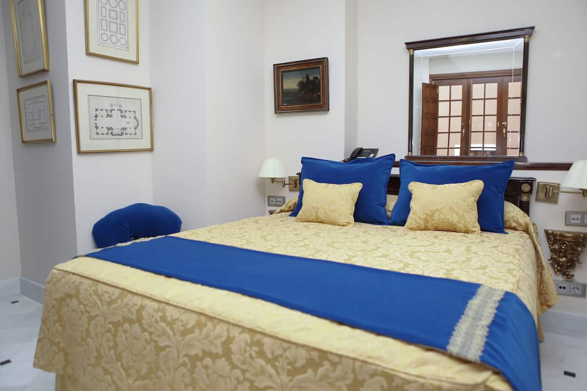 A neatly arranged hotel room with a large bed, a chair, a desk, and a mirror.