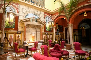 A luxurious lobby with ornate columns, red velvet chairs, and a checkered floor. - Hotel Ateneo Sevilla (Seville)