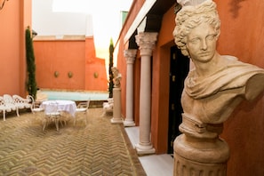 Un patio con una estatua clásica, sillas blancas y una fuente.