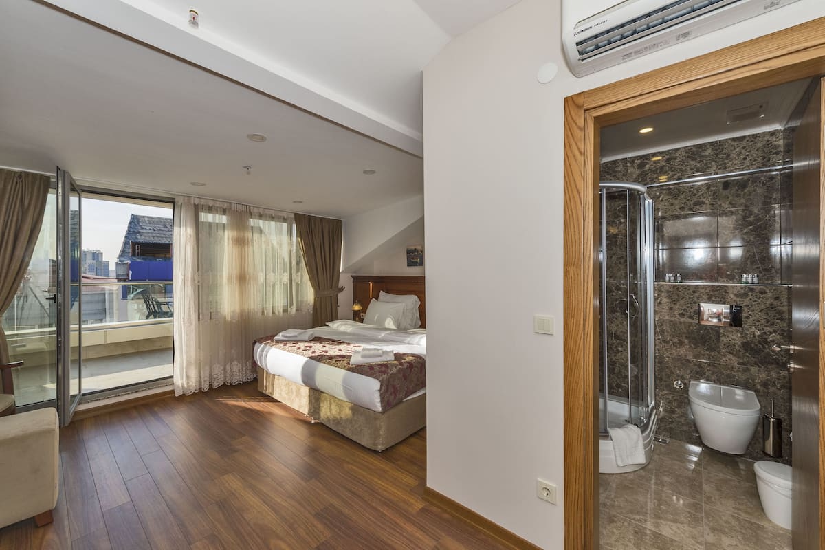 A hotel room with a bed, a glass door leading to a balcony, and a bathroom with a shower and toilet.