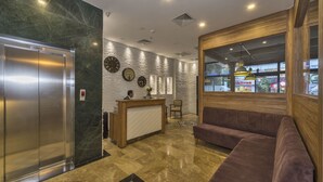 A lobby with a reception desk, a wooden wall with a window, a sofa, and an elevator. - Blisstanbul Hotel (Istanbul)