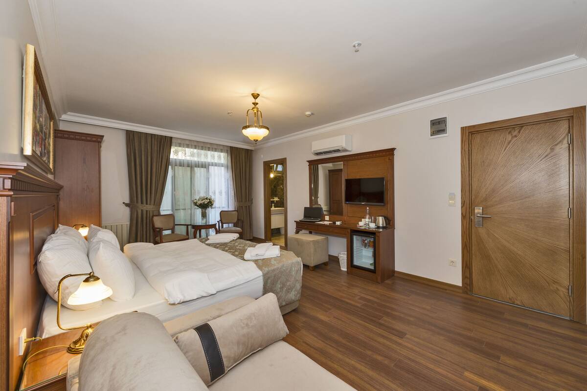 A hotel room with a large bed, a desk with a laptop, a small refrigerator, and a television.